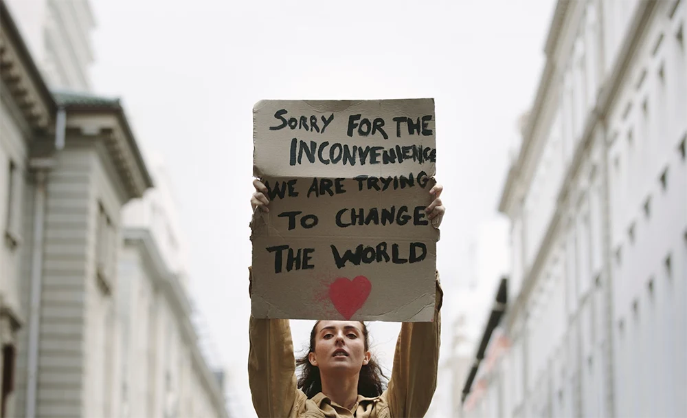 Woman holding protest sign - sorry for the inconvenience, we are trying to change the world.